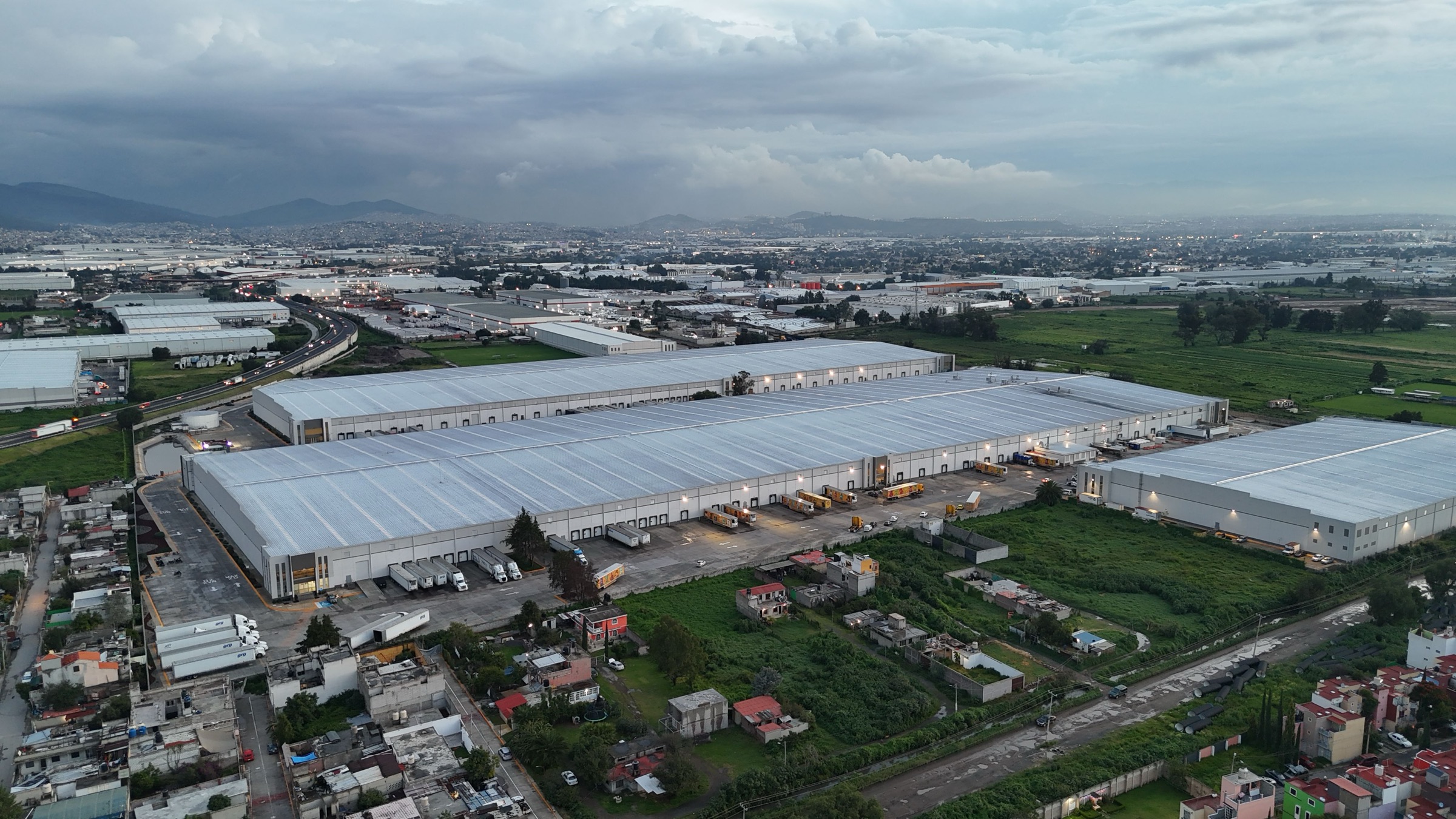 An aerial view at dusk of a large distribution campus, with long rows of dock doors, trailers lined up and a highway running past